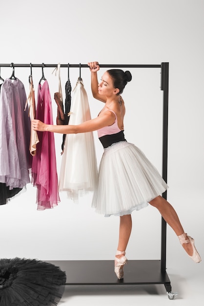 Jonge ballerina die zich op tiptoe bevindt die tutu van hangers kiest