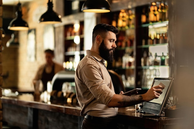 Gratis foto jonge barman met kassa bij toog in een pub.