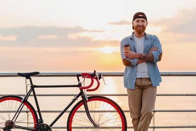 Jonge, bebaarde man die op de fiets reist bij zonsondergang op zee