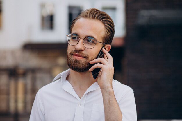 Jonge, bebaarde man die telefoon gebruikt en op straat loopt