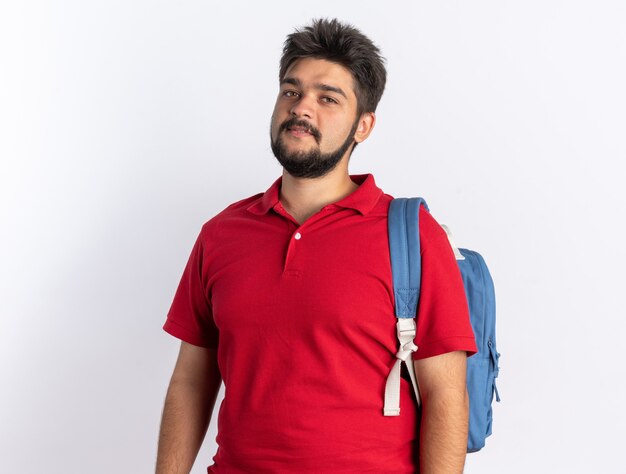 Jonge, bebaarde student in een rood poloshirt met rugzak die er glimlachend zelfverzekerd uitziet