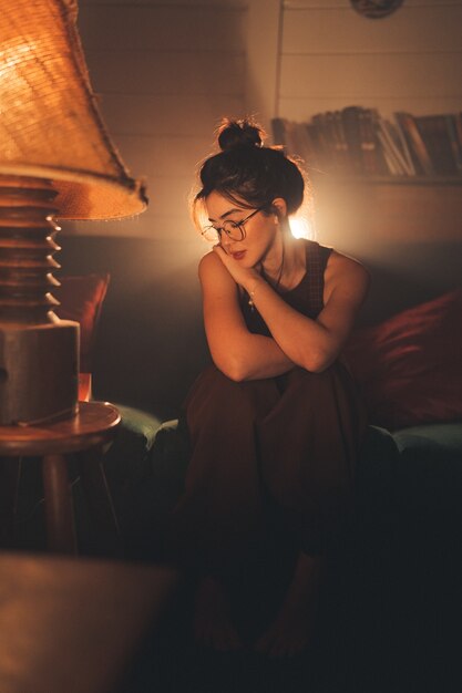 Jonge, bedachtzame vrouw met een bril in een gezellige woonkamer.