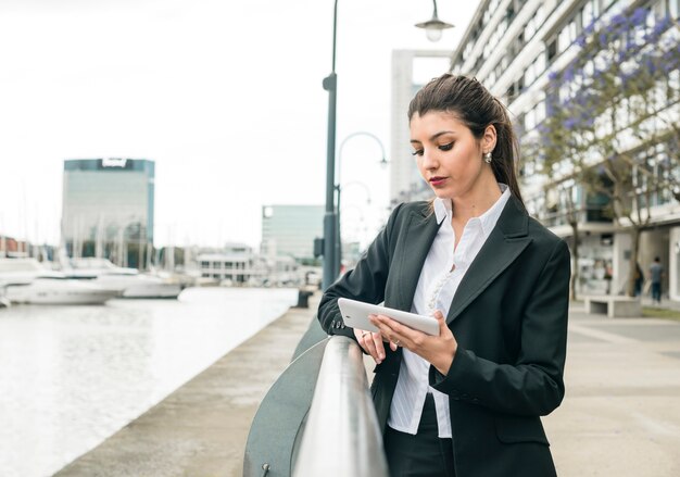 Jonge bedrijfs status dichtbij het traliewerk die op slimme telefoon bij openlucht betrekking hebben