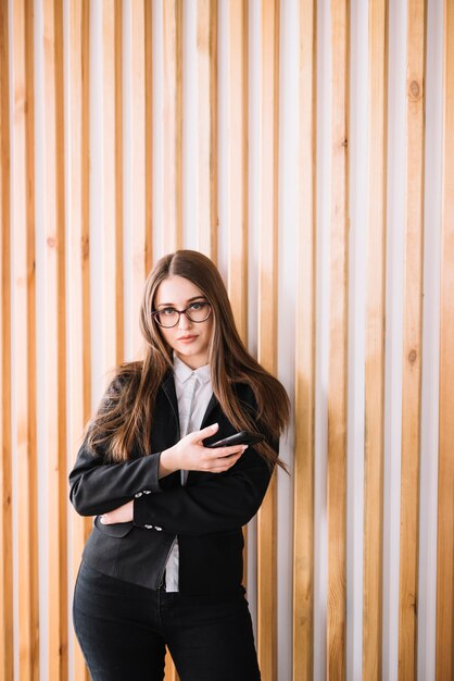 Jonge bedrijfsvrouw die smartphone gebruiken bij houten muur