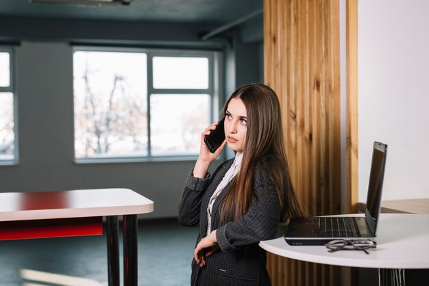 Jonge bedrijfsvrouw die telefonisch bij lijst spreekt