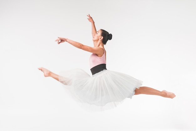 Jonge bevallige vrouwelijke balletdanser die tegen witte achtergrond springt
