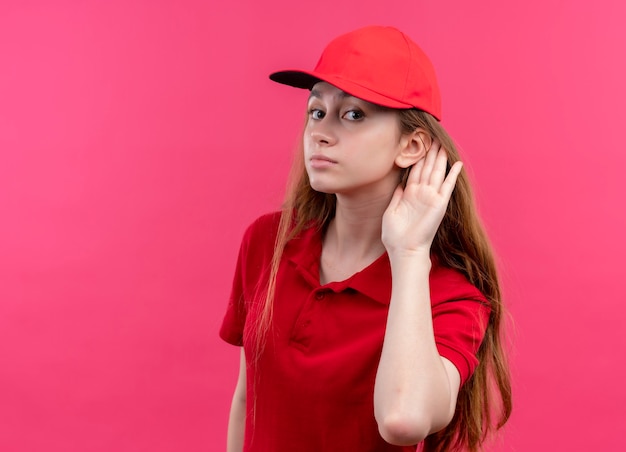 Jonge bezorger in rood uniform kan je niet horen op geïsoleerde roze muur met kopie ruimte