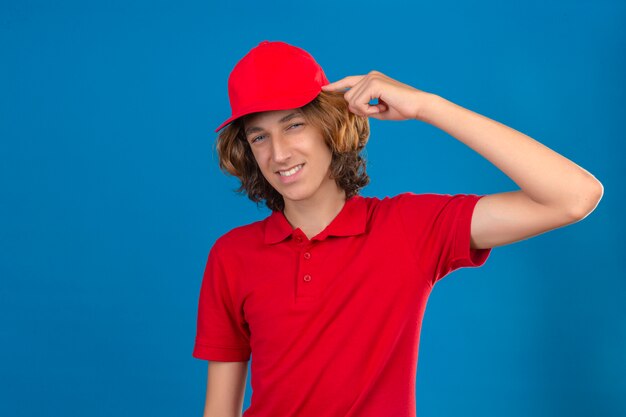 Jonge bezorger in rood uniform wijzende tempel met vinger denken gericht op een taak over geïsoleerde blauwe achtergrond