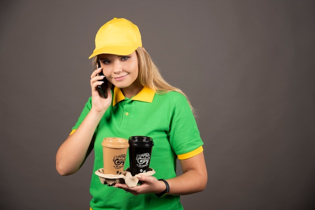 Jonge bezorger met kopjes koffie spreken op smartphone.