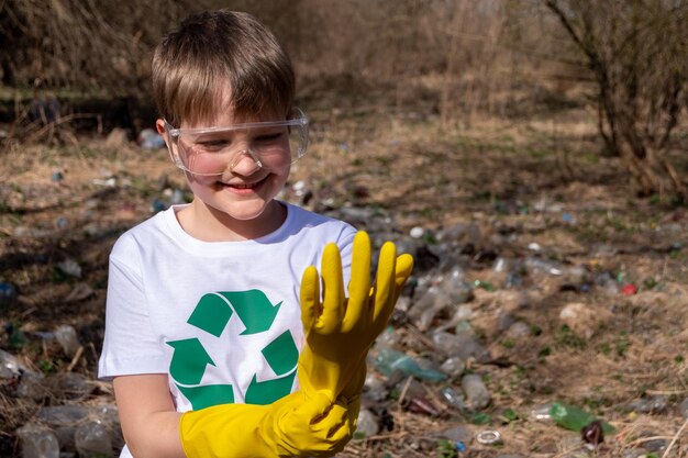 Jonge blanke blanke jongen met een recyclingsymbool op zijn t-shirt en een bril die gele handschoenen aantrekt