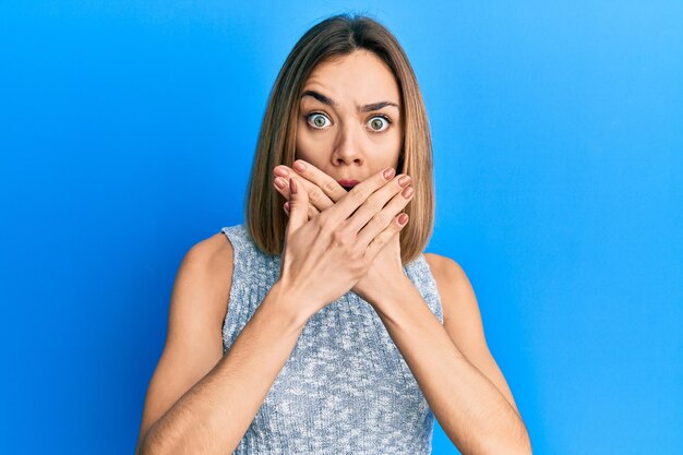 Gratis foto jonge blanke blonde vrouw, gekleed in casual t-shirt, geschokt bedekkende mond met handen voor fout geheim concept