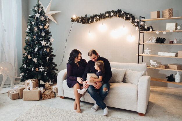 Jonge blanke familie van drie zit samen op de bank naast de kerstboom