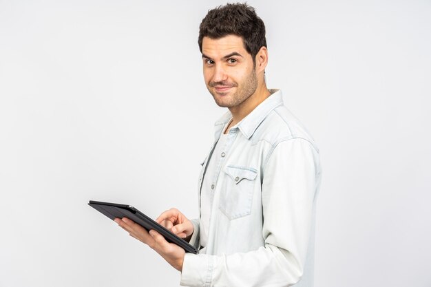 Jonge blanke man die lacht terwijl hij op een tablet tegen een witte muur werkt