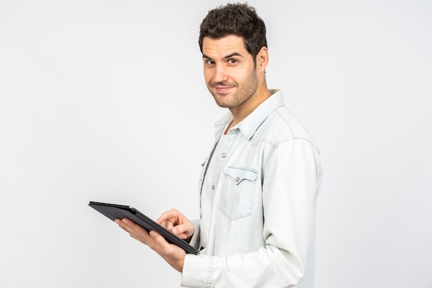 Jonge blanke man die lacht terwijl hij op een tablet tegen een witte muur werkt