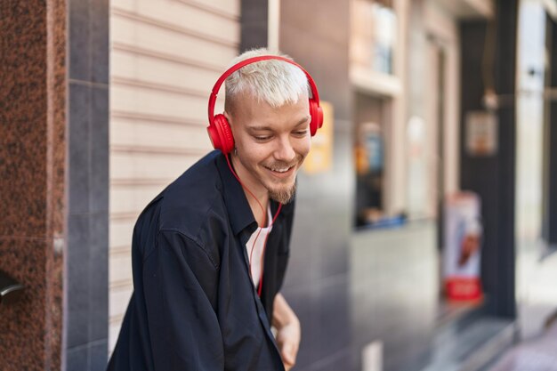 Jonge blanke man glimlachend zelfverzekerd luisteren naar muziek en dansen op straat