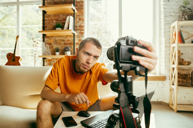 Jonge blanke mannelijke blogger met professionele camera opname videoreview van gadgets thuis.