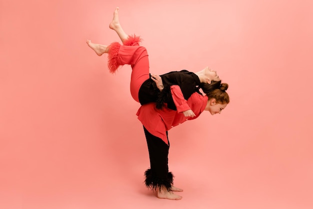 Jonge blanke meisjes spelen in vrijetijdskleding heffen elkaar op op roze achtergrond Leuk concept