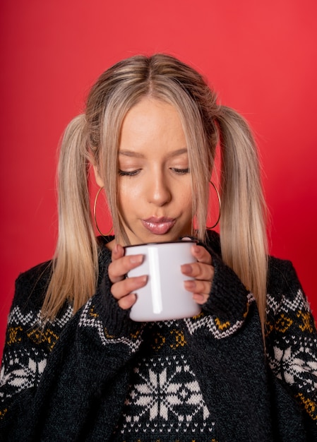 Jonge blanke vrouw in een schattige trui thee drinken zittend tegen een rode muur