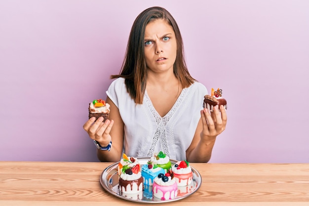 Gratis foto jonge blanke vrouw met cakeplakken geen idee en verward uitdrukking twijfel concept