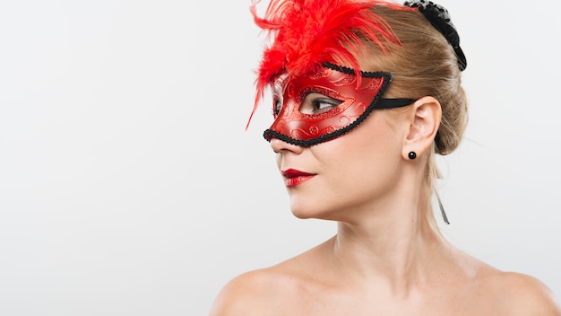 Jonge blonde dame in masker met rode veren