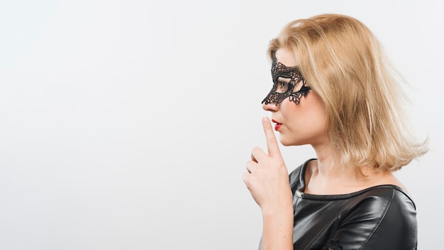 Jonge blonde dame in masker met vinger dichtbij lippen