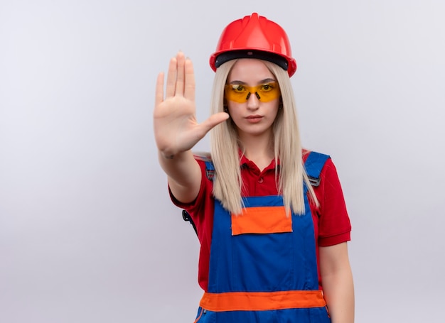 Jonge blonde ingenieur bouwer meisje in uniform dragen veiligheidsbril uitrekken hand gebaren stop op geïsoleerde witte muur met kopie ruimte