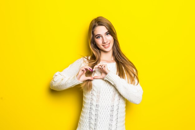 Jonge blonde model op geel is verliefd toont hartteken met haar handen