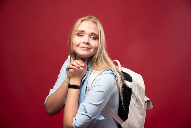 Jonge blonde studentenvrouw met haar rugzak gaat terug naar school en voelt zich heerlijk en gelukkig.