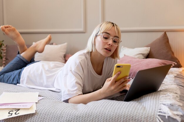 Jonge blonde vrouw die vanuit huis in haar bed werkt