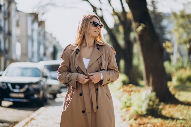 Jonge blonde vrouw in beige jas die op straat loopt