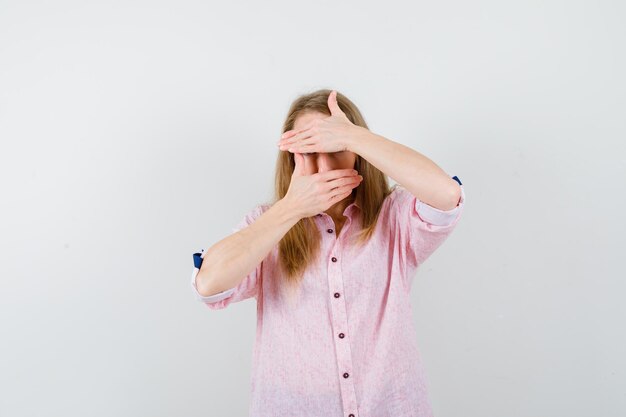 Jonge blonde vrouw in een casual roze shirt dat haar gezicht bedekt