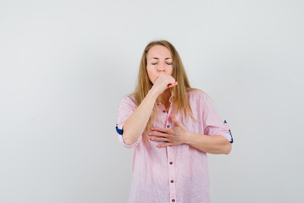 Jonge blonde vrouw in een casual roze shirt hoestend