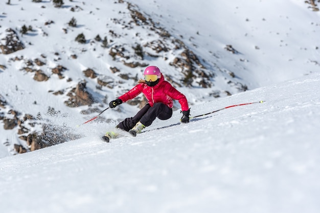 Jonge blonde vrouw in skibril en helm skiën op een besneeuwde berghelling