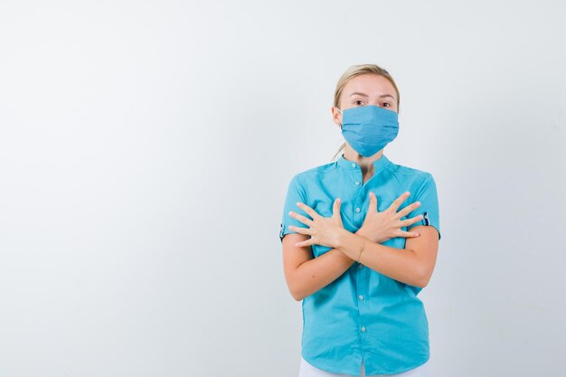 Jonge blonde vrouw in vrijetijdskleding, masker met gekruiste handen geïsoleerd