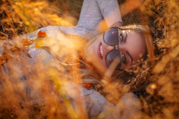 Jonge blonde vrouw in zonnebril liggend in gouden gras.