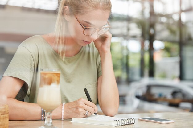 Jonge blonde vrouw met een bril in café