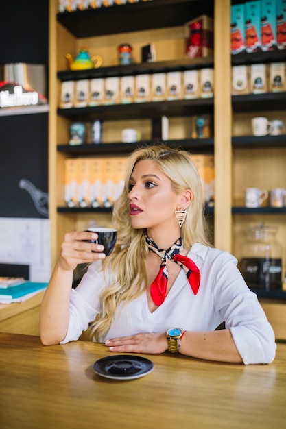 Gratis foto jonge blonde vrouw met een kopje thee in de winkel