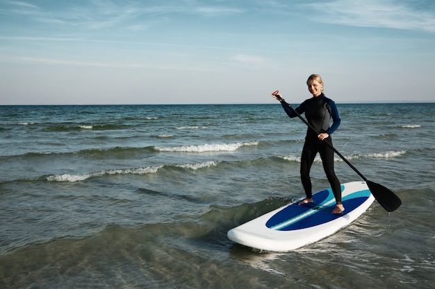Jonge blonde vrouw op paddleboard op zee