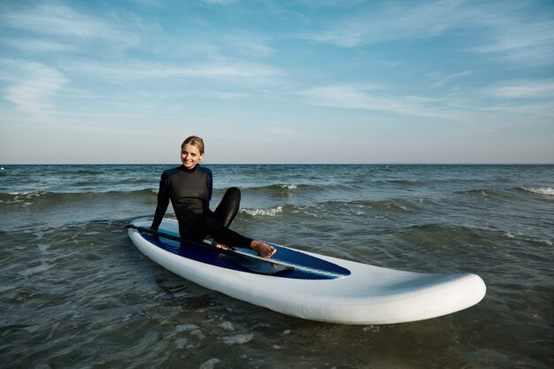 Jonge blonde vrouw op paddleboard op zee