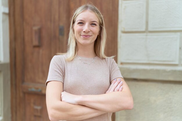 Gratis foto jonge blonde vrouw stond met armen gekruist gebaar op straat