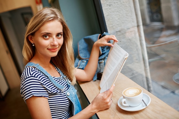 Jonge blonde vrouw zitten in café en lezen
