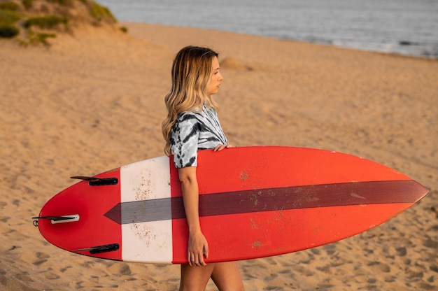 Jonge blonde vrouwelijke surfer wandelen op het strand met haar surfplank