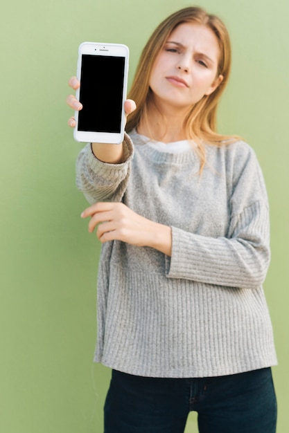 Jonge blondevrouw die haar slimme telefoon tonen tegen groene achtergrond