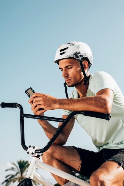 Gratis foto jonge bmxruiter die het telefoon middelgrote schot bekijkt