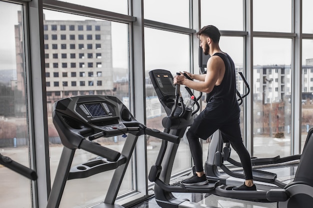 Jonge bodybuilder die cardiotraining uitvoert en naar het venster van de sportschool kijkt