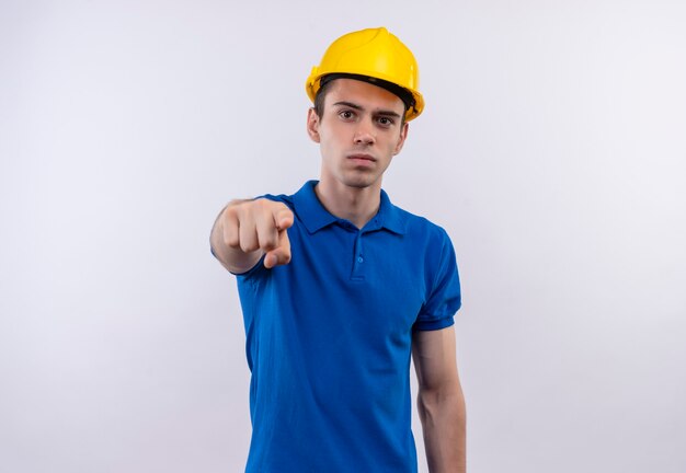Jonge bouwersmens die bouwuniform en veiligheidshelm punten met wijsvinger dragen
