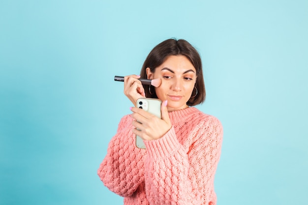 Jonge brunette in roze trui geïsoleerd op blauwe muur