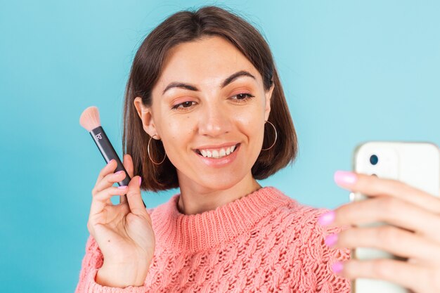 Jonge brunette in roze trui geïsoleerd op blauwe muur