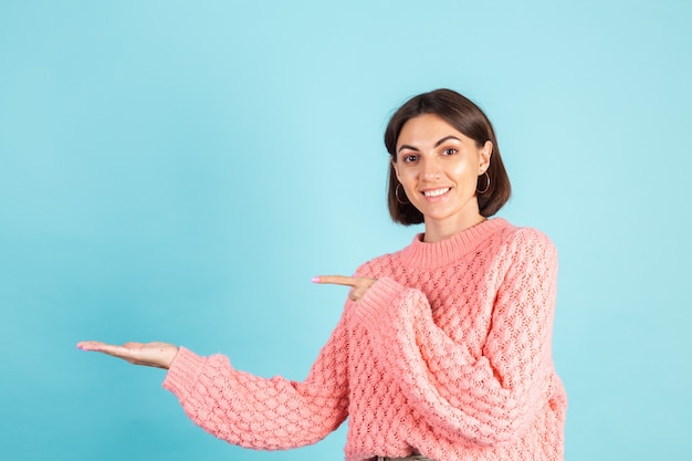 Jonge brunette in roze trui geïsoleerd op blauwe muur