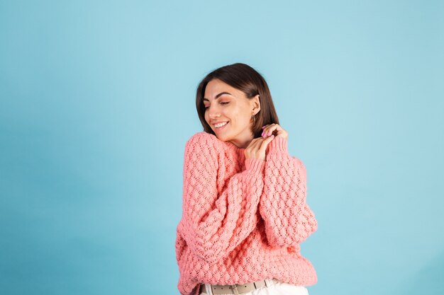 Jonge brunette in warme roze trui geïsoleerd op blauwe muur